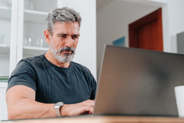 Hombre de unos 50 años que trabaja desde casa mientras toma un café y está en una videollamada en la computadora