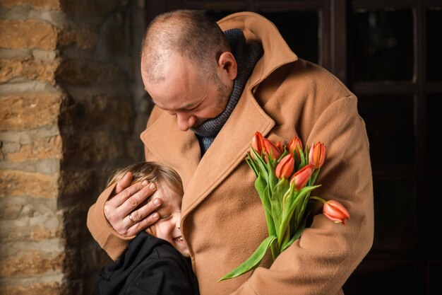 Un hombre abraza a un hijo pequeño y un ramo de flores Día del padre la reunión tan esperada