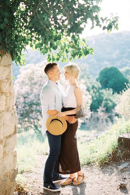 El hombre abraza a la mujer cerca de un muro de piedra contra un fondo de montañas verdes