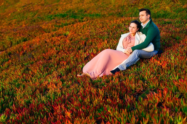 Un hombre abraza a una mujer y se sientan en la hierba y miran a lo lejos.
