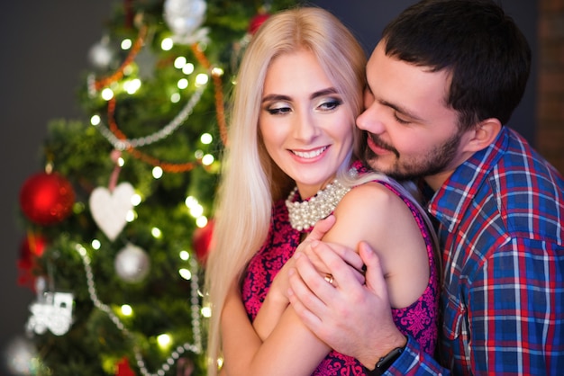El hombre abraza a su joven y bella esposa sobre los hombros durante las vacaciones de Año Nuevo en casa