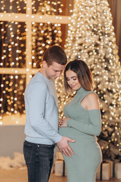 hombre abrazando a mujer embarazada cerca del árbol de Navidad