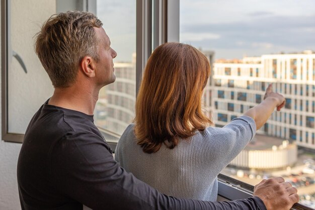 Hombre abrazando a su esposa joven pareja mudándose a nuevos apartamentos la gente mira por la ventana a nuevas casas concepto de nuevas casas nuevo comienzo