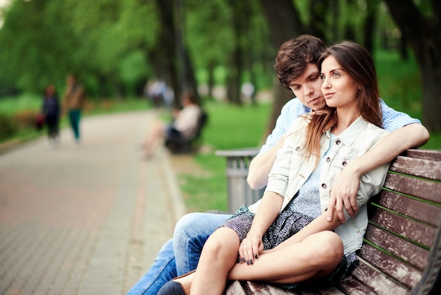 Hombre abrazando a su novia mientras está sentado en un banco en el parque en el verano