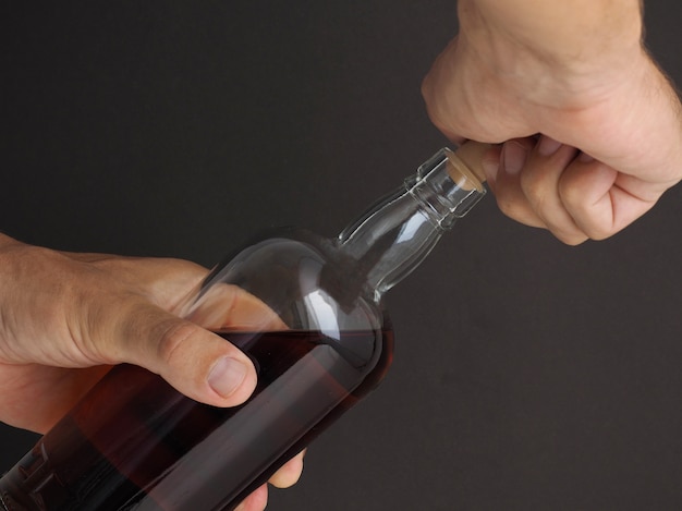 Foto el hombre abre una botella de ron medio borracho. de cerca.