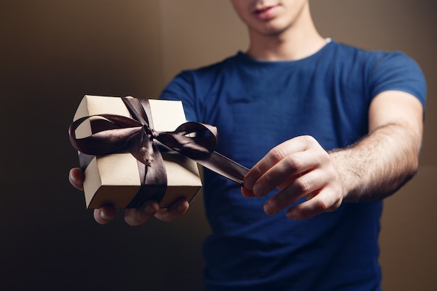 El hombre abre la cinta de regalo sobre fondo marrón