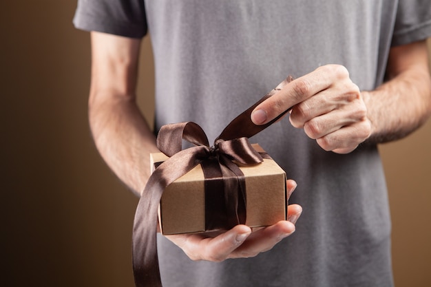 El hombre abre la cinta de regalo sobre fondo marrón