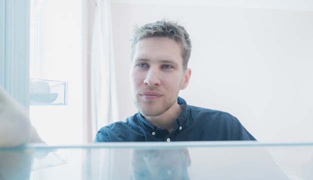 Un hombre abre la nevera para tomar algo de comer, vista desde el interior