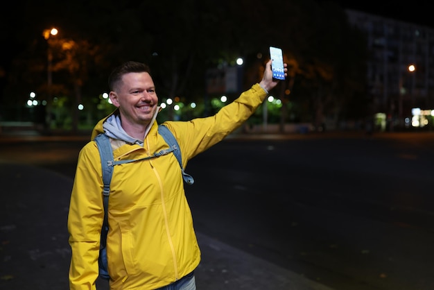 Hombre con abrigo amarillo con mochila azul y teléfono móvil en la mano se encuentra con sus amigos en la calle