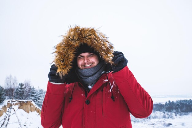 Hombre en abrigo de invierno rojo con capucha de piel campo nevado en el fondo