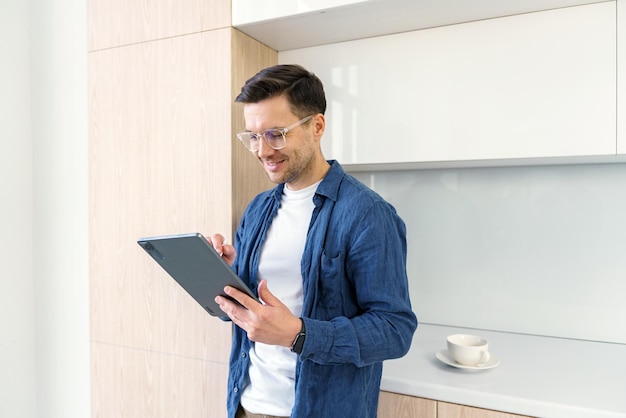 Un hombre absorto examina una tableta en una cocina minimalista su postura casual pero atenta