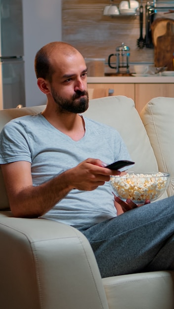 Hombre aburrido cambiando de canales de televisión con palomitas de maíz en hads