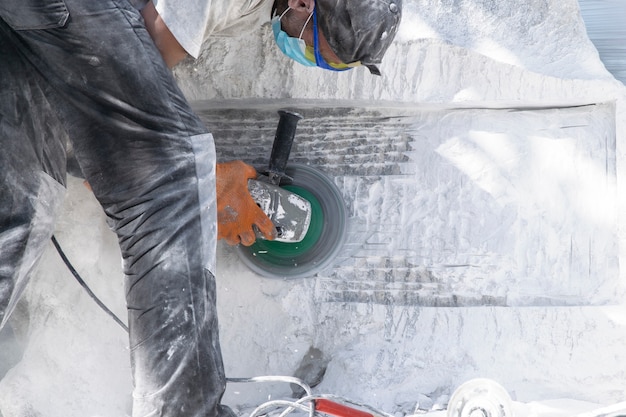 Foto un hombre con accesorios de protección está trabajando en el procesamiento de una gran piedra blanca.