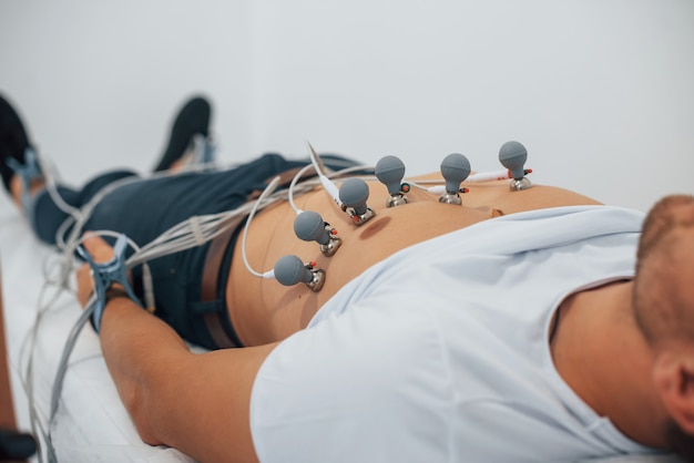 Foto hombre acostado en la cama en la clínica y recibiendo una prueba de electrocardiograma.