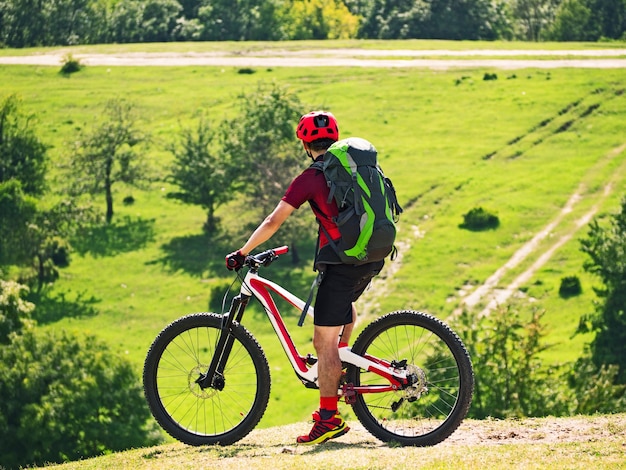 Hombre activo con mochila montando bicicleta de suspensión total en sendero en el fondo natural