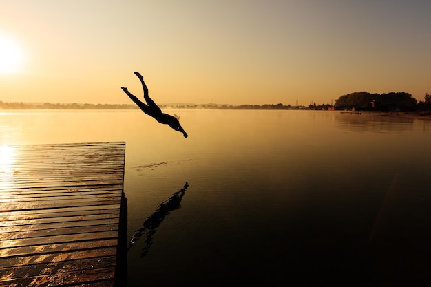 Hombre activo saltando desde el muelle de madera en el lago brumoso