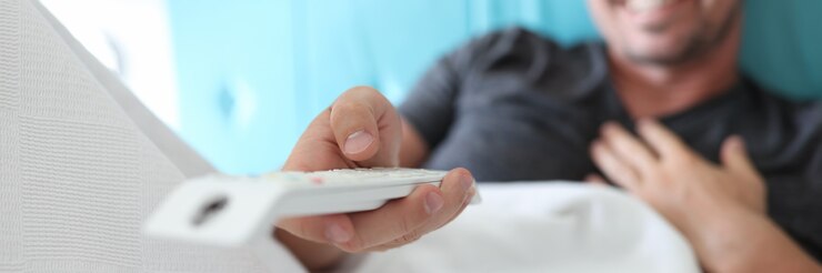 Foto el hombre se acuesta en la cama y tiene el control remoto en sus manos.