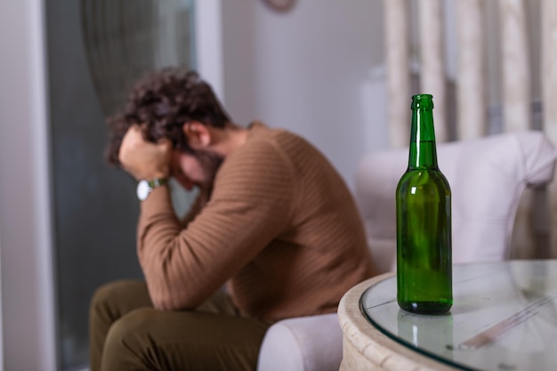 Hombre adicto joven triste deprimido que se siente mal bebiendo cerveza solo en casa, alcohólico bebedor solitario frustrado estresado sufre de adicción al alcohol que tiene problemas, concepto de alcoholismo