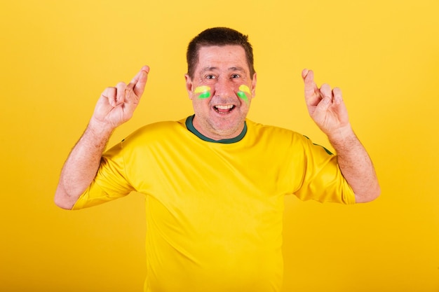 Hombre adulto aficionado al fútbol de brasil dedos cruzados signo de suerte deseando foto de primer plano