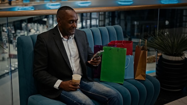 Hombre adulto africano hombre de negocios de mediana edad con bolsas de compras en la tienda del centro comercial con taza de té de café