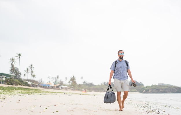 Hombre adulto alegre con bolsa divirtiéndose en la playa tropical