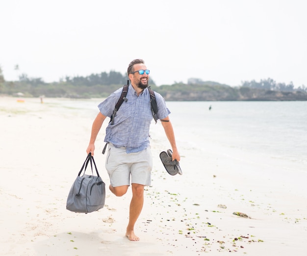 Hombre adulto alegre con bolsa divirtiéndose en la playa tropical