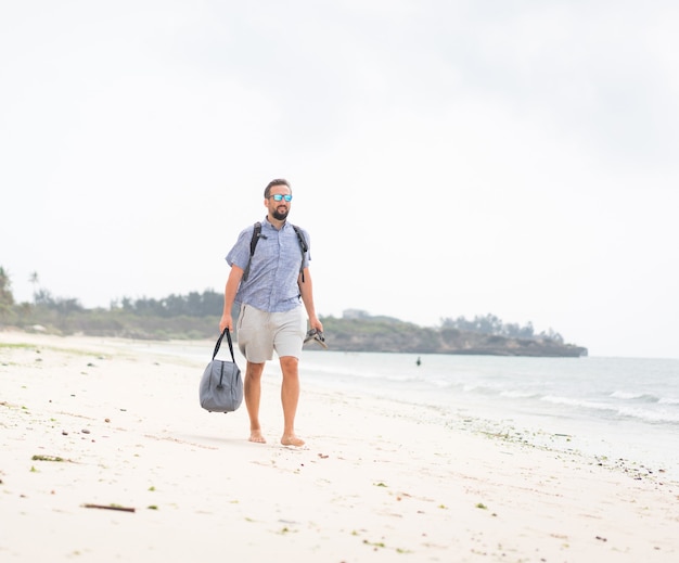 Hombre adulto alegre con bolsa divirtiéndose en la playa tropical