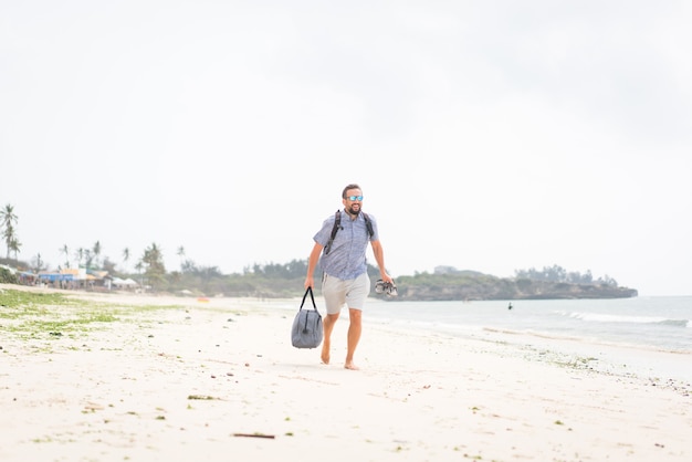 Hombre adulto alegre con bolsa divirtiéndose en la playa tropical