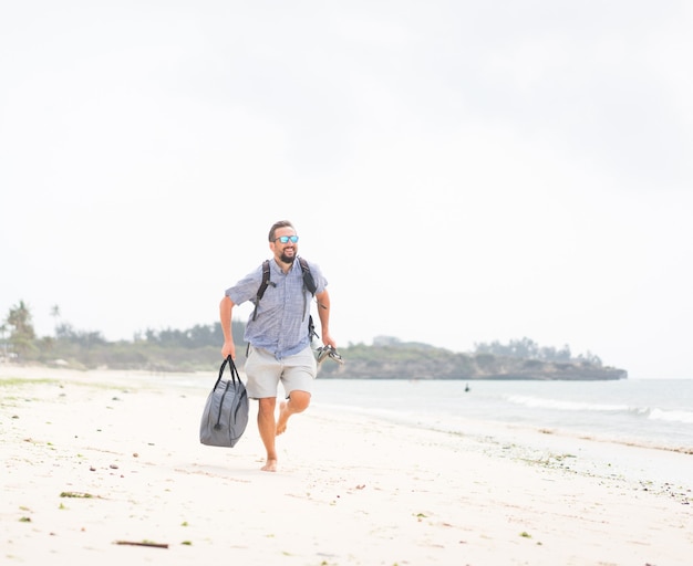 Hombre adulto alegre con bolsa divirtiéndose en la playa tropical