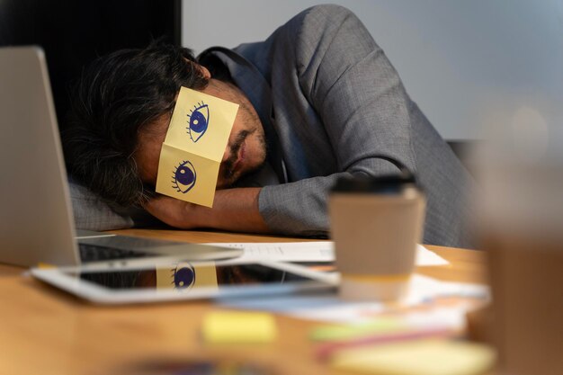 Hombre adulto alegre descansando en la oficina con notas pegajosas en los ojos hombre dormido con pegatinas con ojos pintados en la cara