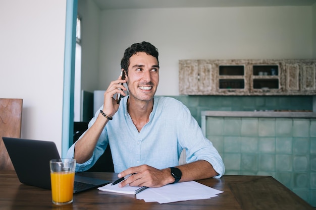 Hombre adulto alegre hablando por teléfono inteligente en la mesa