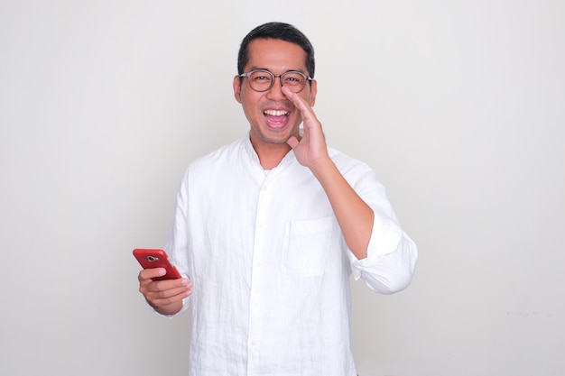 Hombre adulto asiático diciendo algo con expresión emocionada mientras sostiene el teléfono móvil