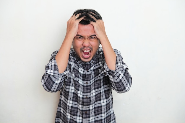 Hombre adulto asiático gritando y agarrándose el cabello mostrando expresión de estrés