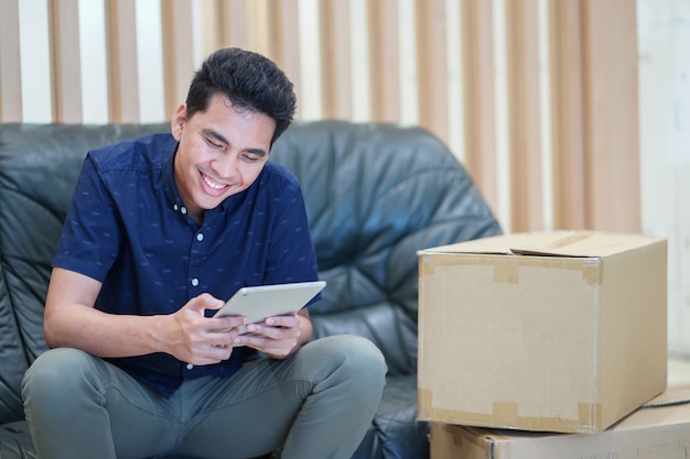 hombre adulto asiático que usa el dispositivo de la tableta para verificar stock de inventario de cajas