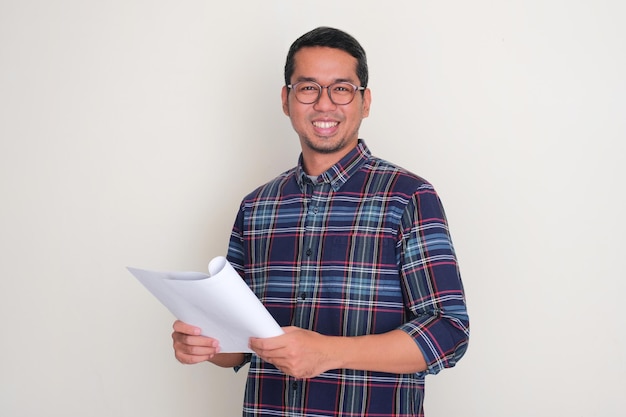 Hombre adulto asiático sonriendo con confianza mientras sostiene un documento de papel