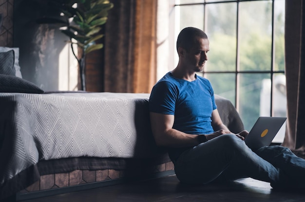 Foto hombre adulto con camiseta azul trabajando en una laptop