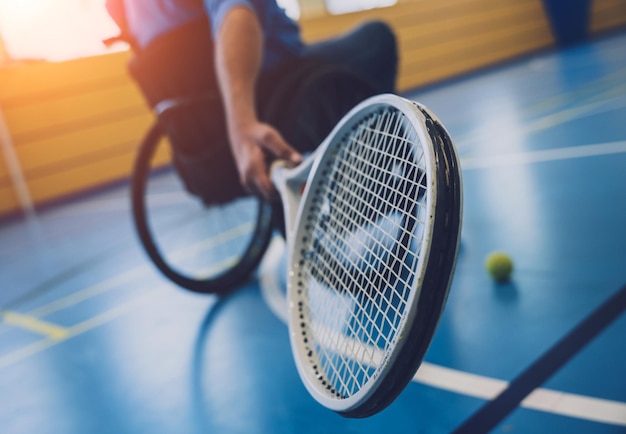 Hombre adulto con discapacidad física que usa silla de ruedas jugando al tenis en una cancha de tenis cubierta