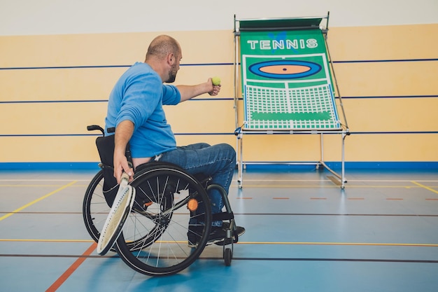 Hombre adulto con discapacidad física en silla de ruedas jugando al tenis en la cancha de tenis cubierta