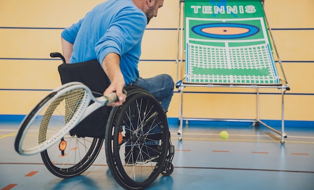 Hombre adulto con discapacidad física en silla de ruedas jugando al tenis en la cancha de tenis cubierta