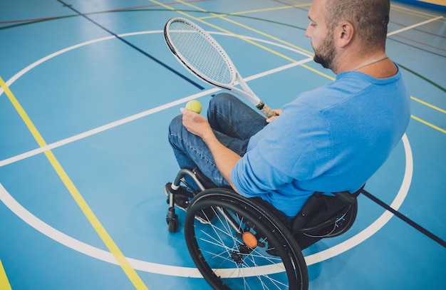 Hombre adulto con discapacidad física en silla de ruedas jugando al tenis en la cancha de tenis cubierta