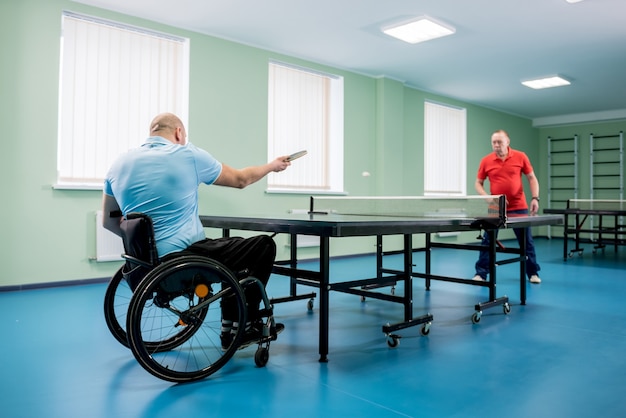 Hombre adulto discapacitado en silla de ruedas jugar al tenis de mesa con su entrenador