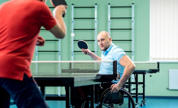 Hombre adulto discapacitado en silla de ruedas jugar al tenis de mesa con su entrenador