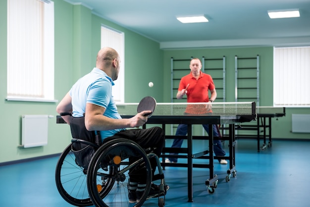 Hombre adulto discapacitado en silla de ruedas jugar al tenis de mesa con su entrenador