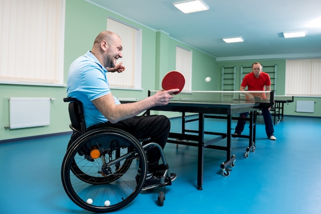 Hombre adulto discapacitado en silla de ruedas jugar al tenis de mesa con su entrenador