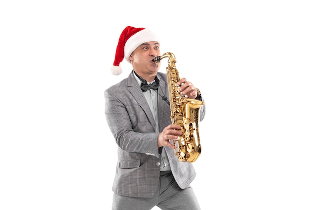 Hombre adulto elegante lleva sombrero de Papá Noel toca el saxofón en la fiesta de año nuevo de fondo blanco