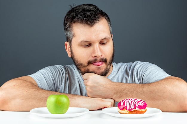 Foto un hombre adulto elige entre una rosquilla y una manzana verde. concepto resistencia a la tentación, comida rápida, comida sana, dieta, cuidado del cuerpo.