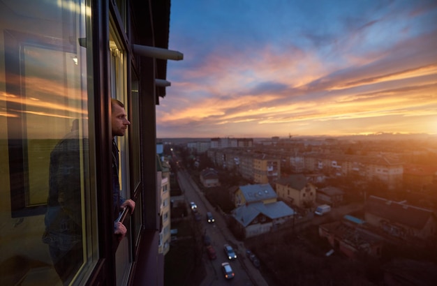 El hombre adulto está parado en el balcón y mirando a lo lejos disfrutando de la puesta de sol Hermoso paisaje de la ciudad