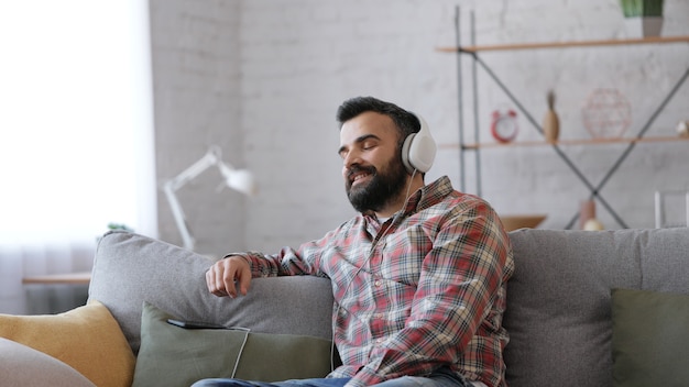 Hombre adulto feliz en auriculares blancos disfruta de escuchar música favorita en el teléfono inteligente con la aplicación de música.