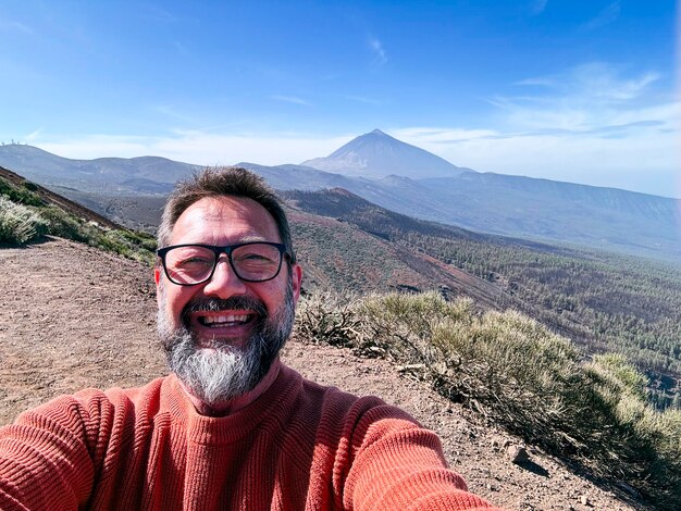 Hombre adulto feliz viajero tomando una foto selfie con vista panorámica en el fondo desde el punto alto de vew Viaje y concepto de felicidad estilo de vida Un hombre maduro alegre usando el teléfono en el ocio al aire libre