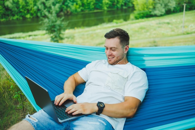 Un hombre adulto guapo relajándose en una hamaca mientras trabaja en una computadora portátil durante una caminata de un día al aire libre Recreación en la naturaleza con trabajo remoto